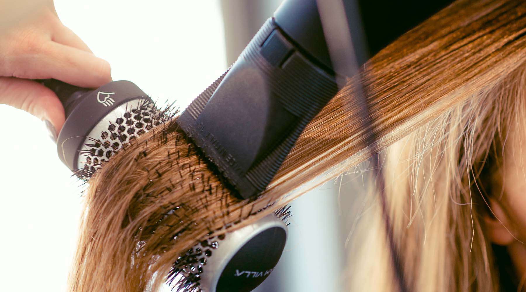 Professional hair stylist blow drying hair using the Sam Villa Artist Series Blow Dryer and Thermal Round Brush for smooth volume and control