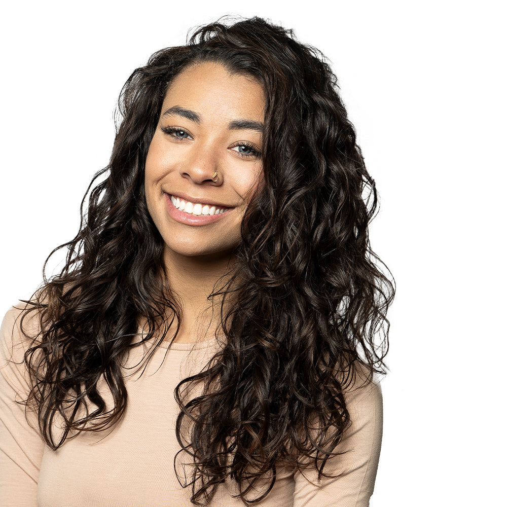 Brunette model with curly hair and nose ring smiling in front of white background.