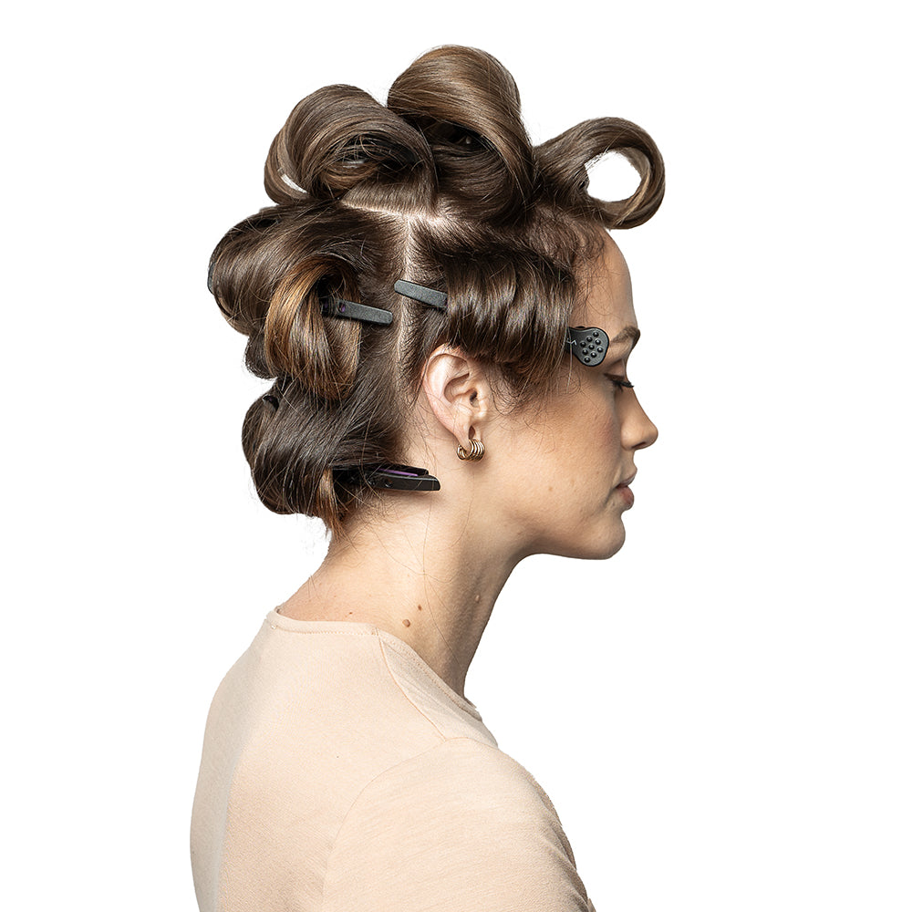 A woman with medium-length brown hair, styled in sections with clips for curling, seen in profile against a white background.
