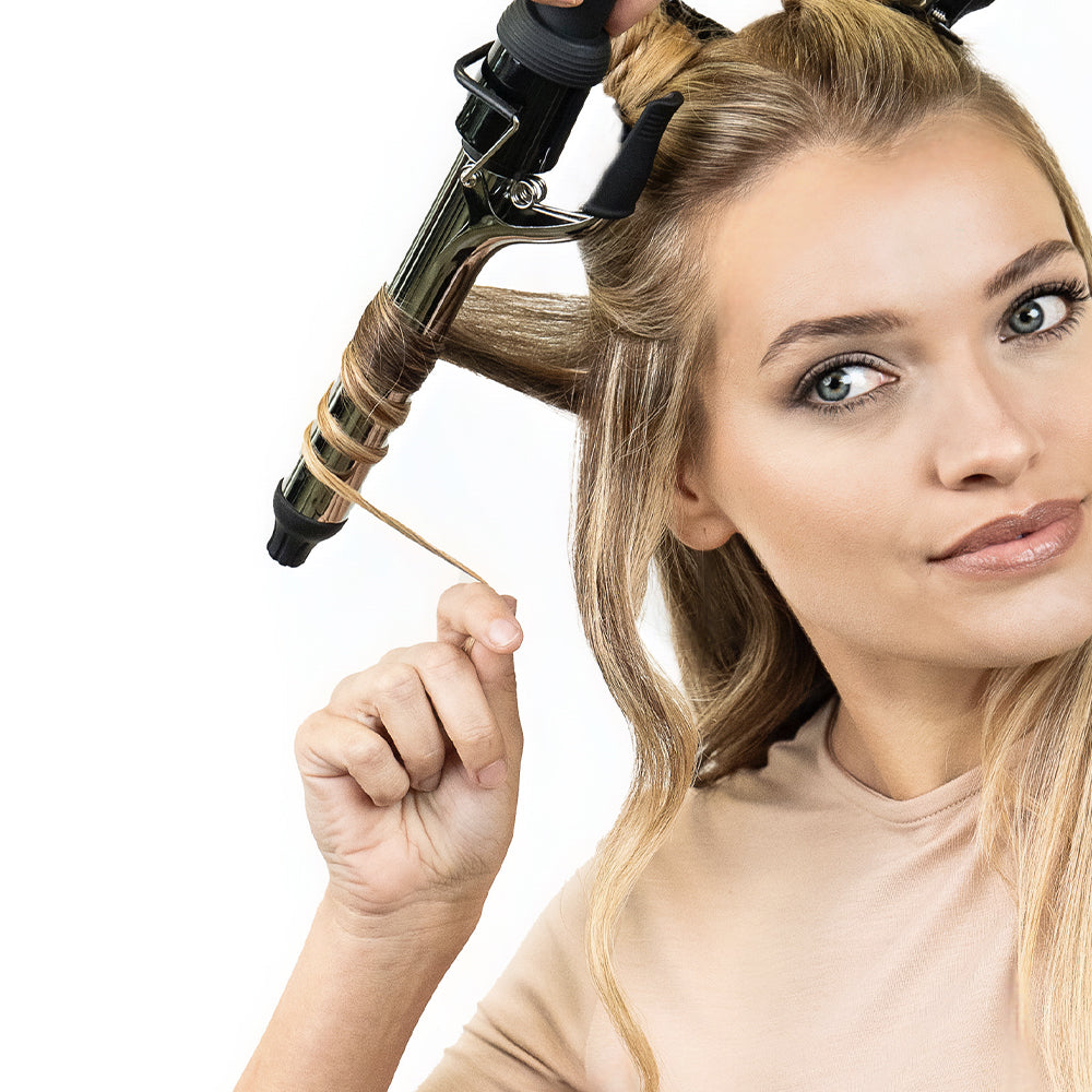 Blonde woman using a Sam Villa curling iron to curl her hair, demonstrating a hair curling technique with a strand wrapped around the barrel.