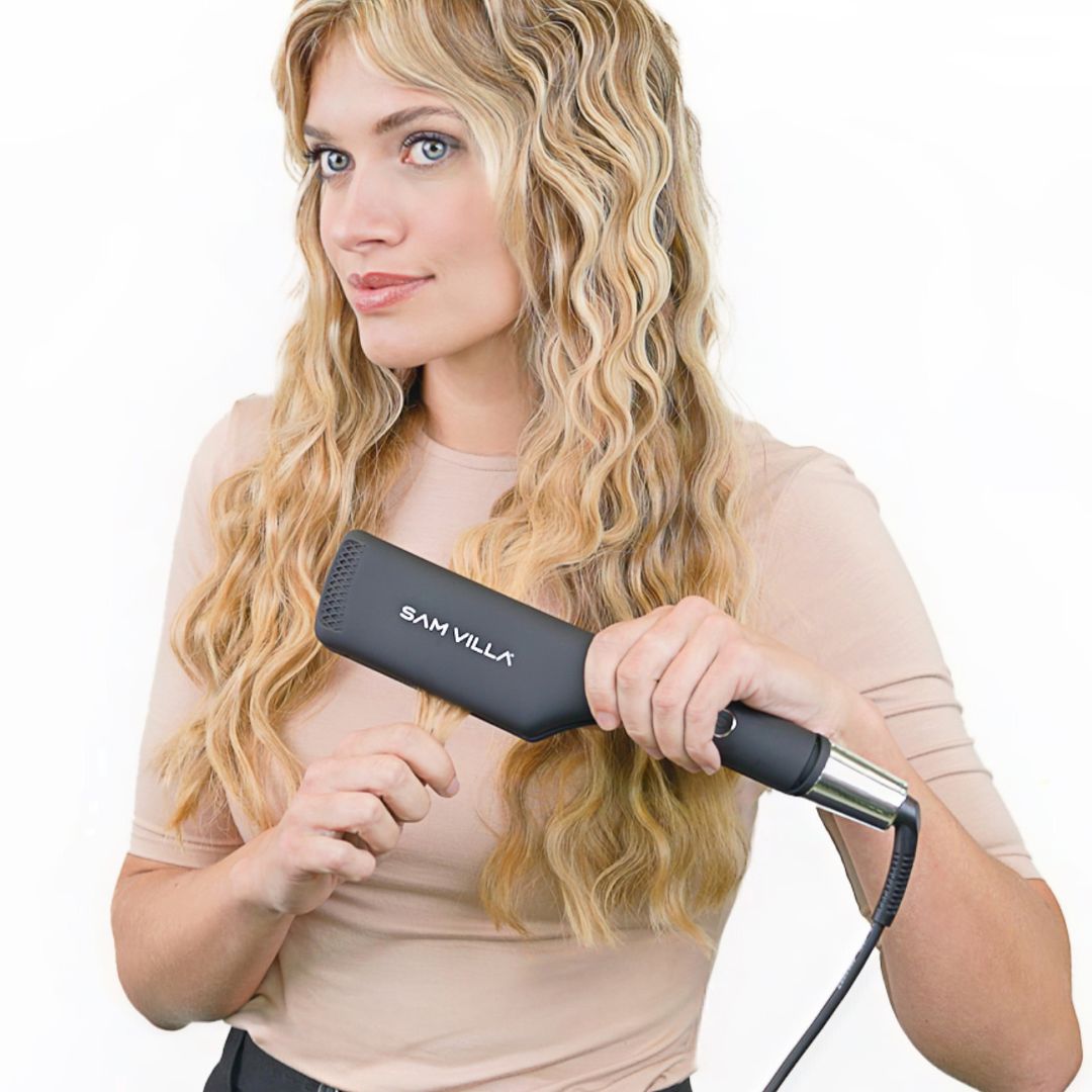 Blonde woman using Sam Villa appliance to style hair in front of white background